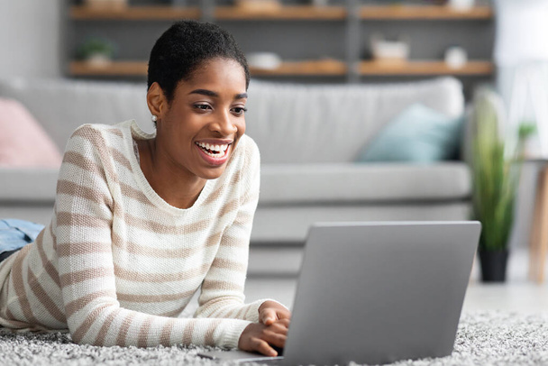 Vrolijke Afro-Amerikaanse dame ontspannen met laptop computer thuis - Foto, afbeelding