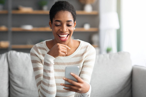 Aplikacja randkowa online. Młody czarny samotny kobieta za pomocą smartfona w domu - Zdjęcie, obraz