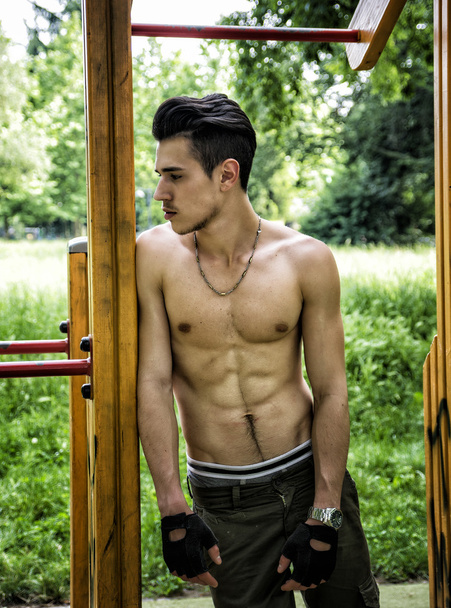 Handsome shirtless young man exercising in outdoor gym in park - Photo, Image