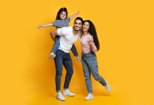 Wesoła bliskowschodnia rodzina trojga bawiących się razem na żółtym tle - Zdjęcie, obraz