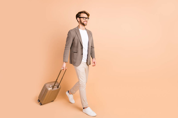 Full size profile side photo of charming cheerful man go empty space good mood travel isolated on pastel beige color background - Φωτογραφία, εικόνα