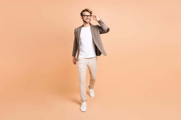Full size photo of attractive dreamy young man walk look empty space smile isolated on beige color background - Valokuva, kuva