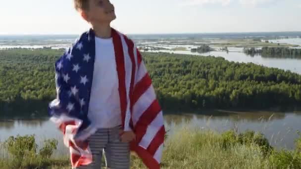 Blondine jongen zwaaien nationale VS vlag buiten boven de blauwe hemel aan de oever van de rivier - Video