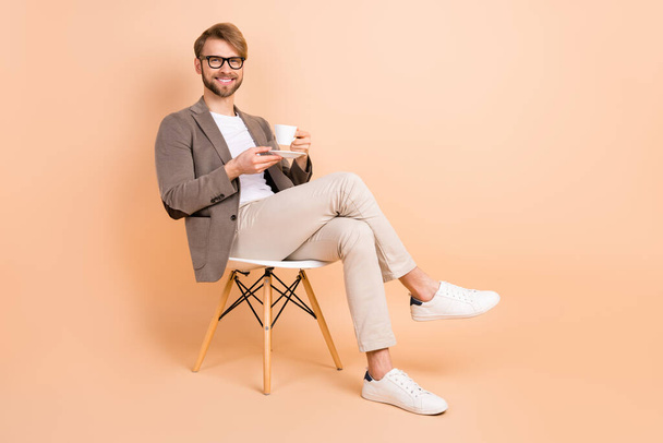 Full size photo of happy handsome attractive charismatic man in glasses relaxing drink tea isolated on beige color background - Valokuva, kuva