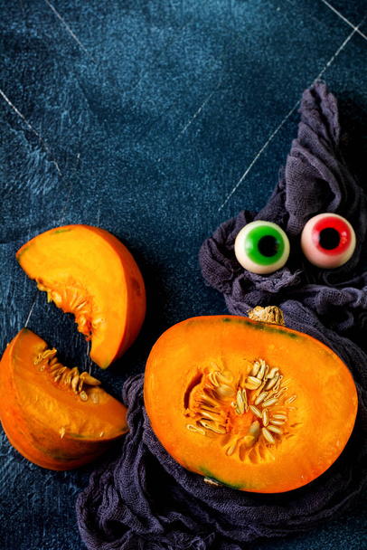 Halves of raw organic pumpkin or butternut squash decorated with candy eyes on blue slate, stone or concrete background. Top view. Halloween holiday concept. Top view with copy space. - Zdjęcie, obraz