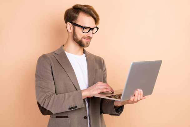 Profile photo of impressed nice blond hair man hold laptop wear spectacles grey jacket isolated on beige background - Foto, afbeelding