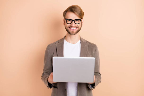 Photo of optimistic nice blond hair man hold laptop wear spectacles grey jacket isolated on beige background - Valokuva, kuva