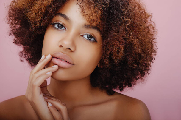 Portrait de beauté d'une belle jeune femme afro-américaine avec un regard mystérieux sur la caméra et mettant ses doigts sur son visage - Photo, image