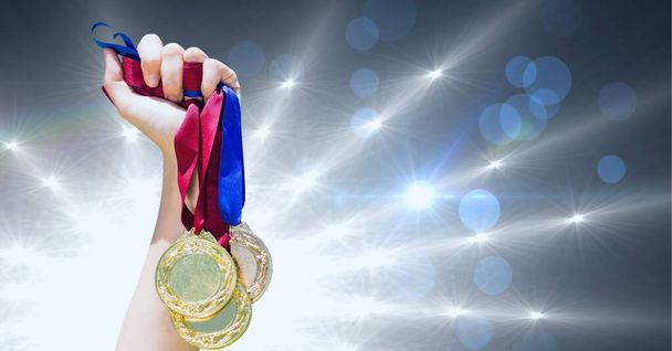 Close up of hand holding multiple medals against shining star lights and spots of light. sports tournament and competition concept - Foto, Bild