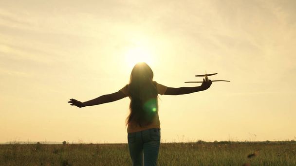 Ребенок мечтает быть пилотом самолета, летящего в небе к солнцу, ребенок бежит в закат, любит бегать на природе, девушка играет на открытом воздухе, чувствует свободу игры - Фото, изображение