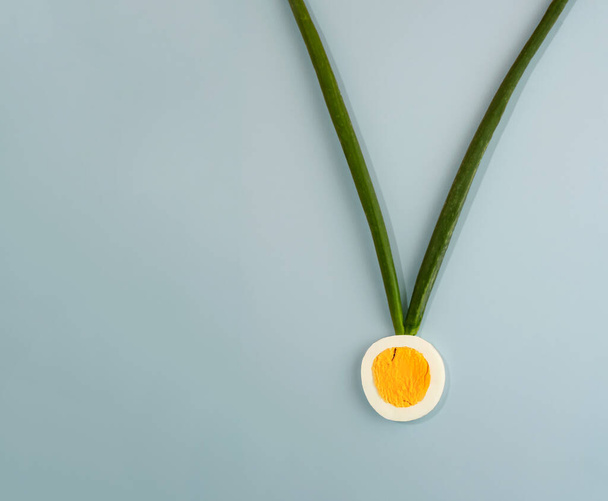Gold medal made of sliced egg and green onion leaves lay down on grey background. Horizontal flat lay composition with copy space, minimal creative concept - Фото, изображение