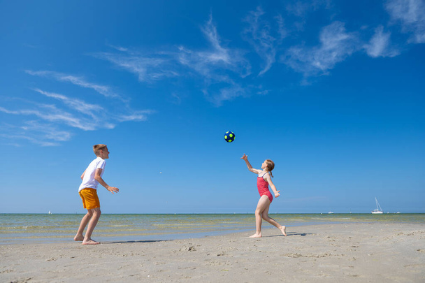 Happy children playing with ball on beach at summer sunny day with blue sky on background - 写真・画像