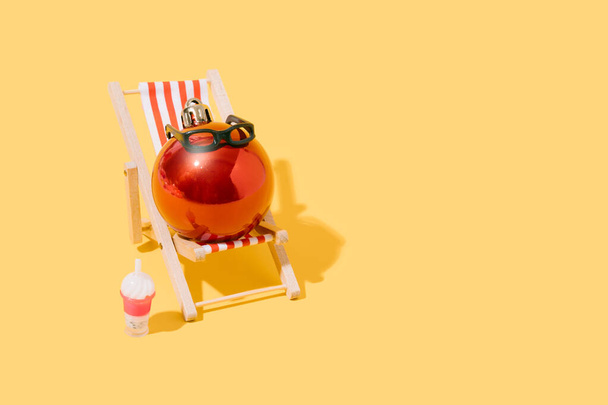 A christmas ball sunbathing on a beach chair. concept of summer, travel and christmas. 3d illustration. copy space - Photo, Image
