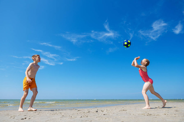 Happy children playing with ball on beach at summer sunny day with blue sky on background - Foto, Imagen