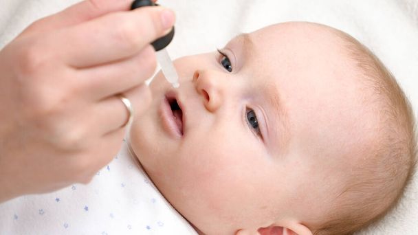 Closeup of little baby boy taking vitamin D from eyedropper. Concept of newborn healthcare and vaccination. - Photo, image