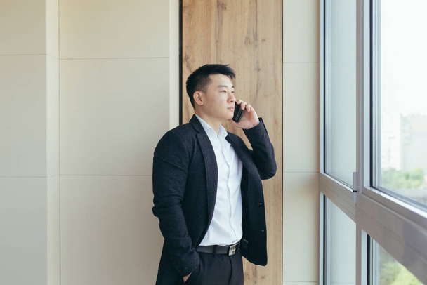 serious boss asian businessman talking on the phone in a modern office center, makes a working call to colleagues - Fotó, kép