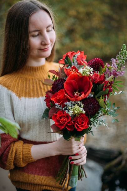 Portret młodej pięknej kobiety z bukietem kwiatów w parku. Dziewczyna gospodarstwa bukiet czerwonych kwiatów w jej rękach na tle jesiennej przyrody - Zdjęcie, obraz