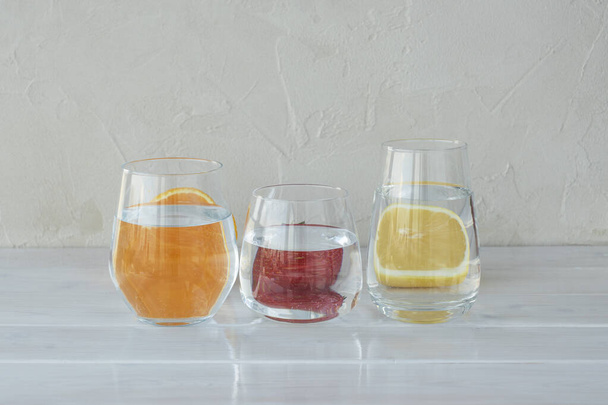 Cutted orange, lemon and strawberry behind transparent glasses with water, ditortion, optical deformation, creative disign. Vitamin drinks concept - Foto, Imagem