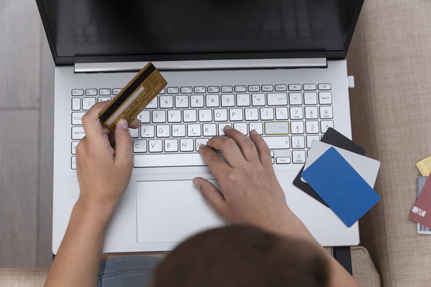 Top view of boy 's hands holding credit card near keyword of laptop, zakupy online, bezpieczeństwo w Internecie - Zdjęcie, obraz