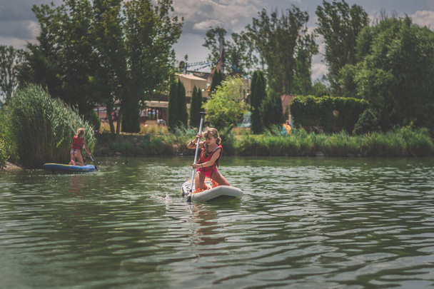 muchacha joven en chaleco inflable rojo de la seguridad que reman en el tablero de la paleta en la superficie del agua en día soleado caliente del verano en naturaleza verde al aire libre - Foto, imagen