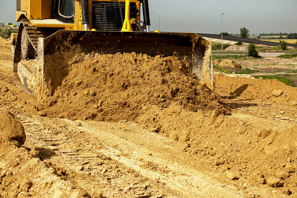 Proces budowy dróg asfaltowych. Poziomy buldożera i kompakty gleby gliny do podstawy autostrady. Roboty ziemne w letni dzień. - Zdjęcie, obraz