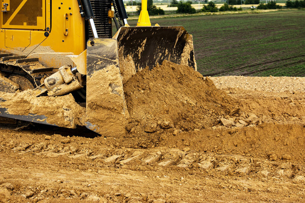 Proceso de construcción de asfalto. La excavadora nivela y compacta el suelo arcilloso para la base de la carretera. Trabajos de tierra en un día de verano. - Foto, imagen