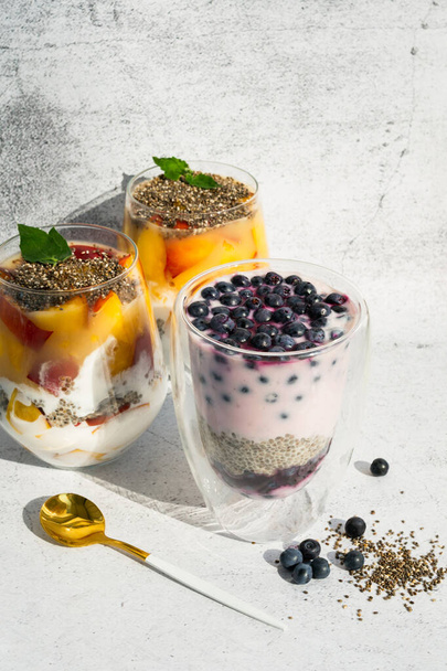 Still life of sliced fruit vegetable milk desserts in glass jar. Organic sweet chia seed superfood pudding. Fresh dairy sweet blueberries and peach fruit breakfast on concrete background. Vegan food - Foto, Imagen