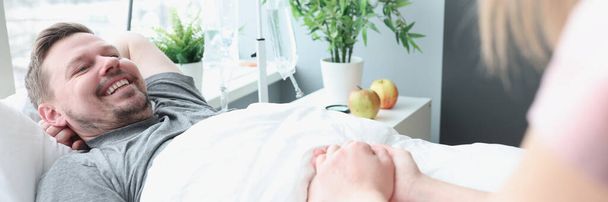 Sorrindo homem encontra-se na cama do hospital sua mão é realizada pela mulher - Foto, Imagem