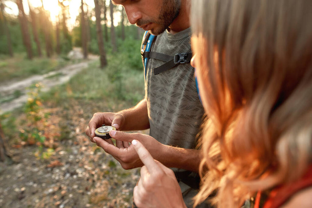 Young couple of tourists holding a compass and looking for direction navigation while walking together in the forest - Foto, Imagem