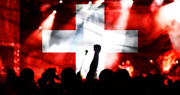 Футбольні уболівальники, які підтримують Швейцарію - натовп, що святкує на стадіоні з піднятими руками проти прапора Швейцарії. - Фото, зображення