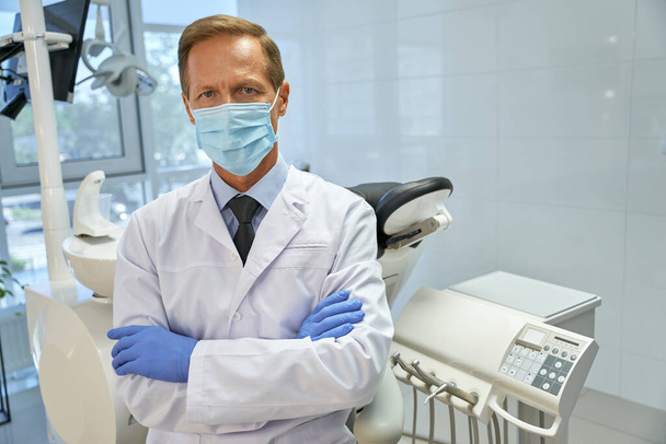 Professionele tandheelkundige chirurg in masker poseren in zijn kliniek - Foto, afbeelding