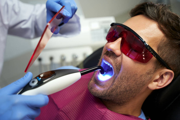 Young man at dental appointment having treatment with blue light - Foto, Bild