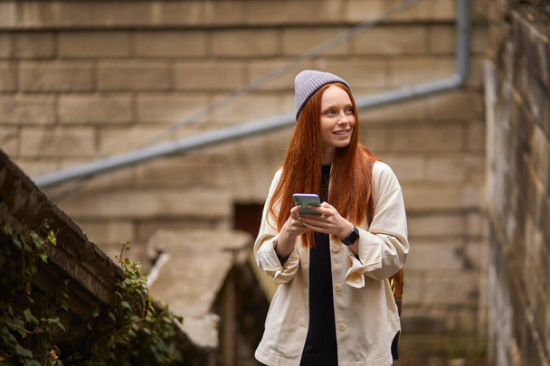Young redhead woman walking in city and using smartphone, browse the Internet - Foto, immagini