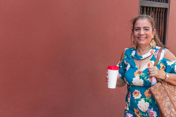 Зріла жінка з кавою, що йде на відкритому повітрі в місті або місті
 - Фото, зображення