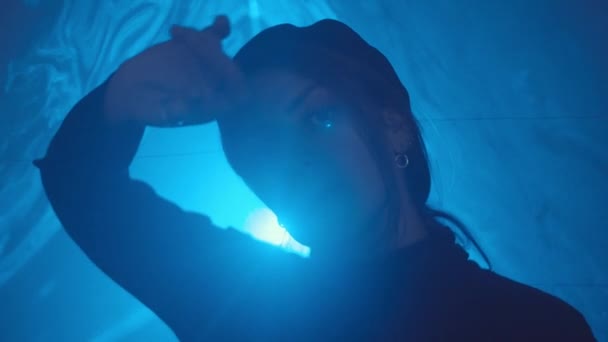 Portrait of young charming woman standing in blue laser tunnel in dark studio, moving her hands and looking at camera - Imágenes, Vídeo