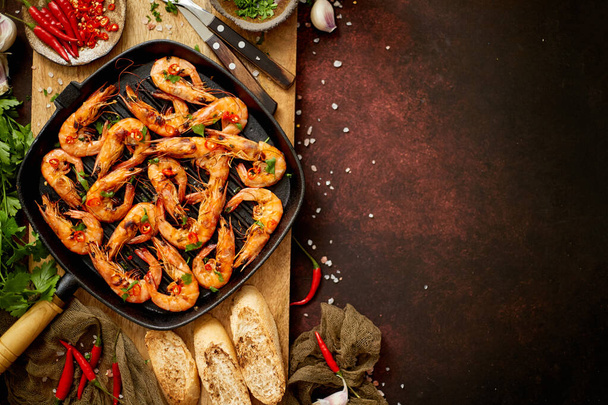 Tasty appetizing roasted shrimps prawns with spices on pan with ingredients on rusty background - Photo, Image