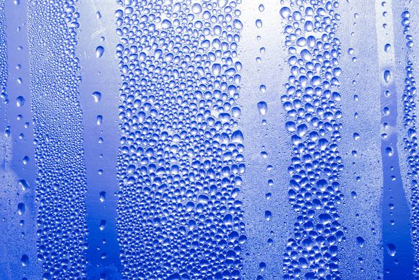L'eau bleue tombe sur le verre. Condensation sur la surface transparente  - Photo, image