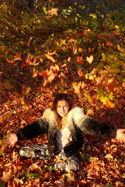 Прекрасная девочка, бросающая листья в воздух во второй половине дня - Фото, изображение