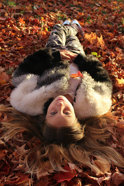 Serious young pretty teen girl laying in autumn background leaves in gold red and yellows leaves  - Photo, Image