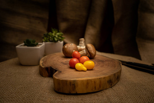 Close-up of cherry tomatoes and portobello mushrooms on a tree slice with burlap cloth background. - Fotoğraf, Görsel