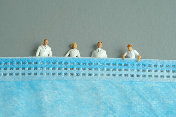 Miniature people toy figure photography. A group of medics including doctor and nurse lying down on a face mask. Medical staff dies due to corona virus concept. Image photo - Photo, Image