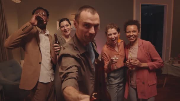 POV medium slowmo van vrolijke groep van multi-etnische vrienden met huisfeest samen Man toasten met fles bier naar de camera en iedereen heeft plezier - Video
