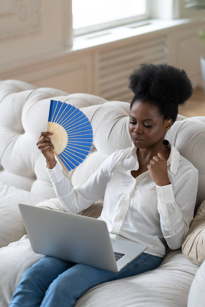 Afro üzleti nő szenved hőguta ül a nappaliban otthon a integető ventilátor - Fotó, kép