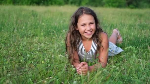 Feliz niña linda acostada en la hierba al aire libre - Imágenes, Vídeo