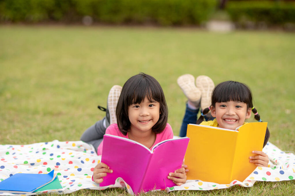 two beautiful little girls reading books in the garden , sitting on grass. The concept of education and friendship. - Fotoğraf, Görsel