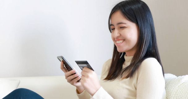 Γυναίκα κάθεται στον καναπέ και χρησιμοποιώντας έξυπνο τηλέφωνο και πιστωτική κάρτα για online ψώνια - Φωτογραφία, εικόνα