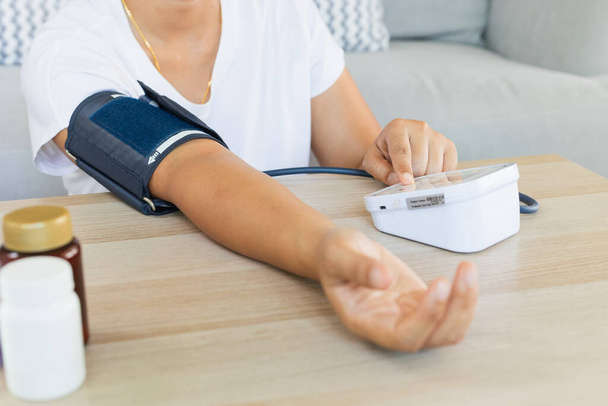 Aasialainen nuori nainen tarkistaa verenpainetta ja sykettä digitaalisella painemittarilla itse kotona. Terveys ja lääketieteellinen käsite. - Valokuva, kuva