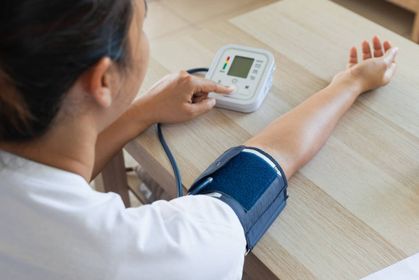 Mujer joven asiática está comprobando la presión arterial y la frecuencia cardíaca con manómetro digital por sí misma en casa. Concepto de salud y medicina. - Foto, Imagen