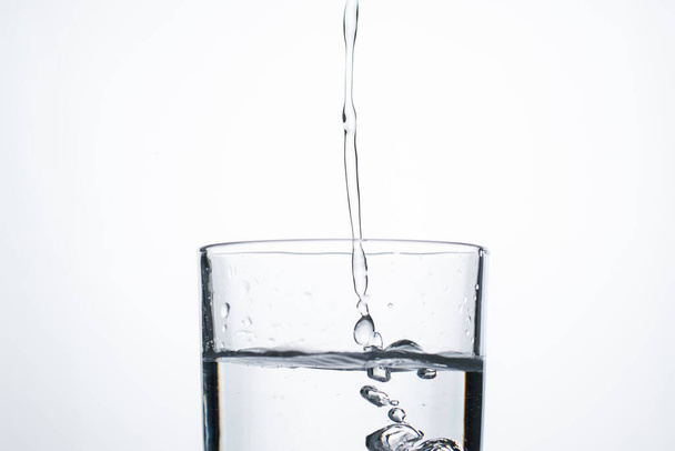 Strumień wody lub alkoholu wlewa się do szklanki z rozpryskami i bąbelkami, przestrzeń kopiowania. - Zdjęcie, obraz