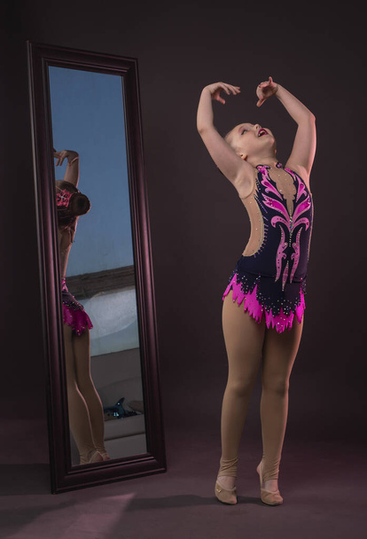 Little girl pretending and dreaming to be gymnast. Junior kid near mirror in costume - Foto, imagen